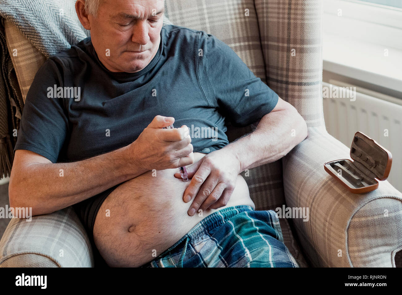 Senior man with diabetes is injecting insulin into his belly at home. Stock Photo