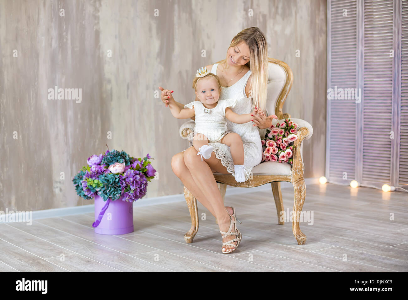 Portrait of mother and daughter lovely hugging each other posing on retro chair with bouquet of flowers Stock Photo