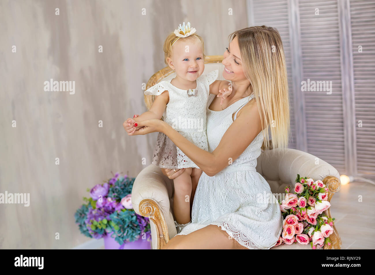 Portrait of mother and daughter lovely hugging each other posing on retro chair with bouquet of flowers Stock Photo