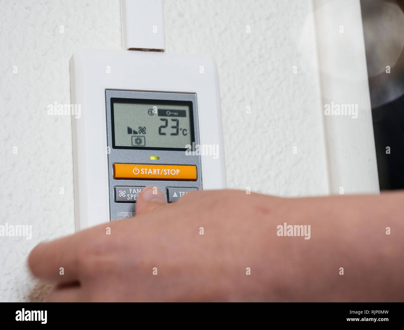 Detail of woman hand adjusting a wall mounted thermostat temperature for the room AC air conditioning system Stock Photo