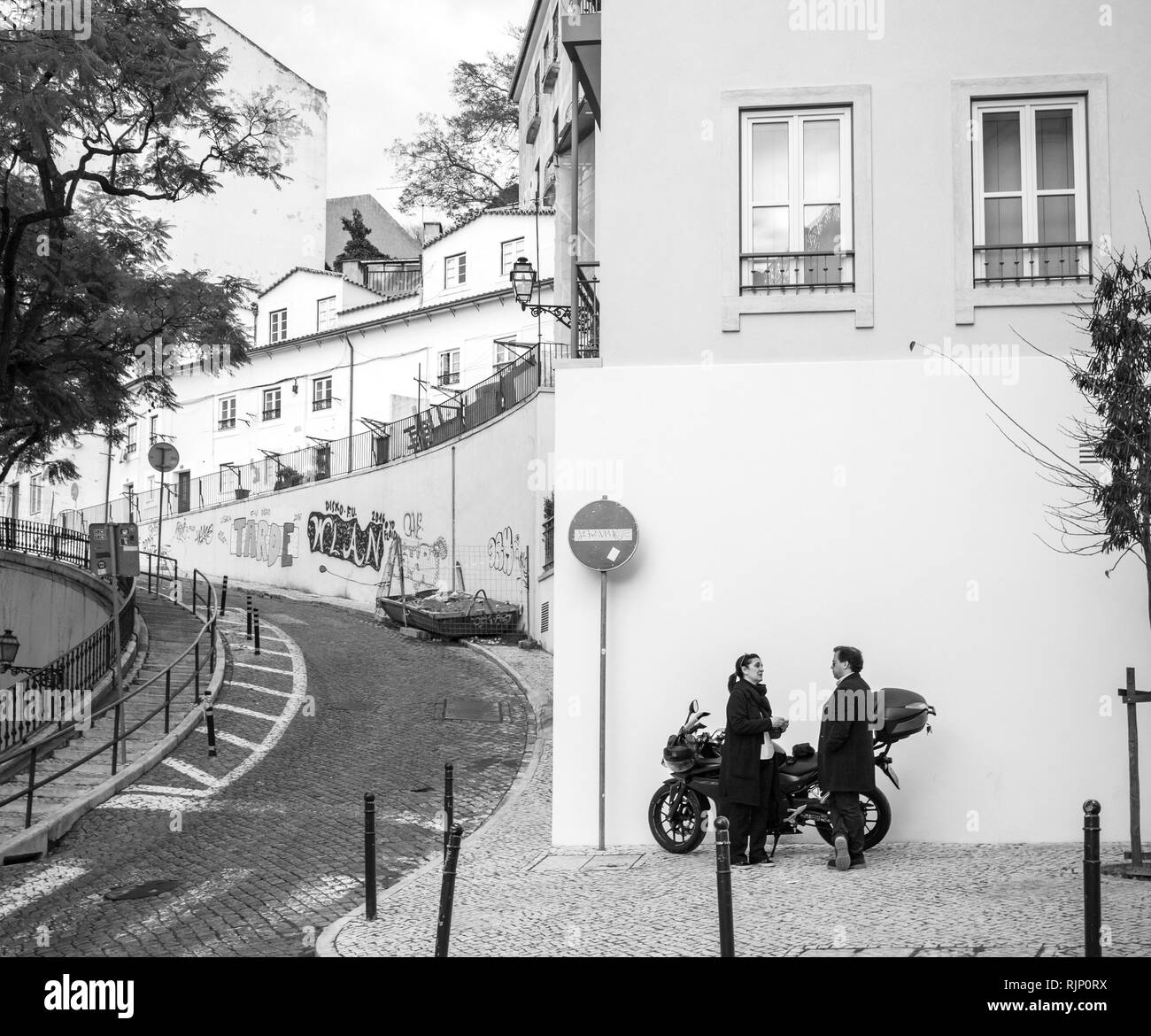 LISBON, PORTUGAL - FEB 9, 2018: Side view of adult man and woman standing on paved street near motorcycle and talking against white wall Stock Photo
