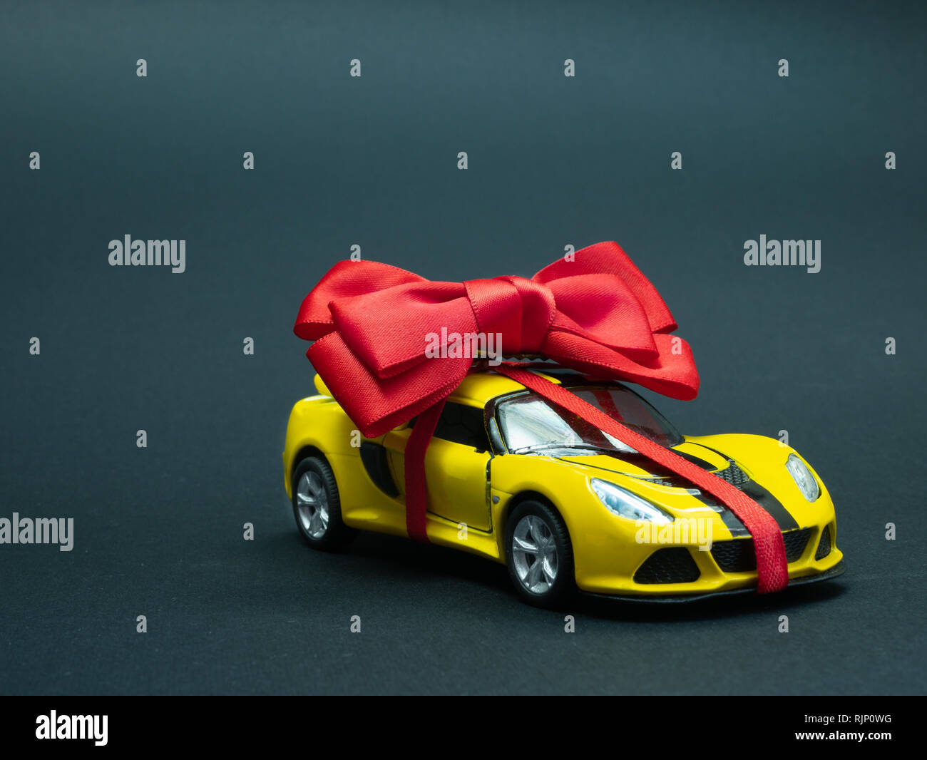 closeup small toy yellow sport car with ribbon and bow on black dark