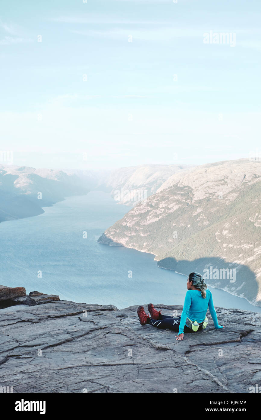 A girl hiker resting and enjoying the view on top of the Pulpit Rock / Preikestolen or Prekestolen in Norway Stock Photo