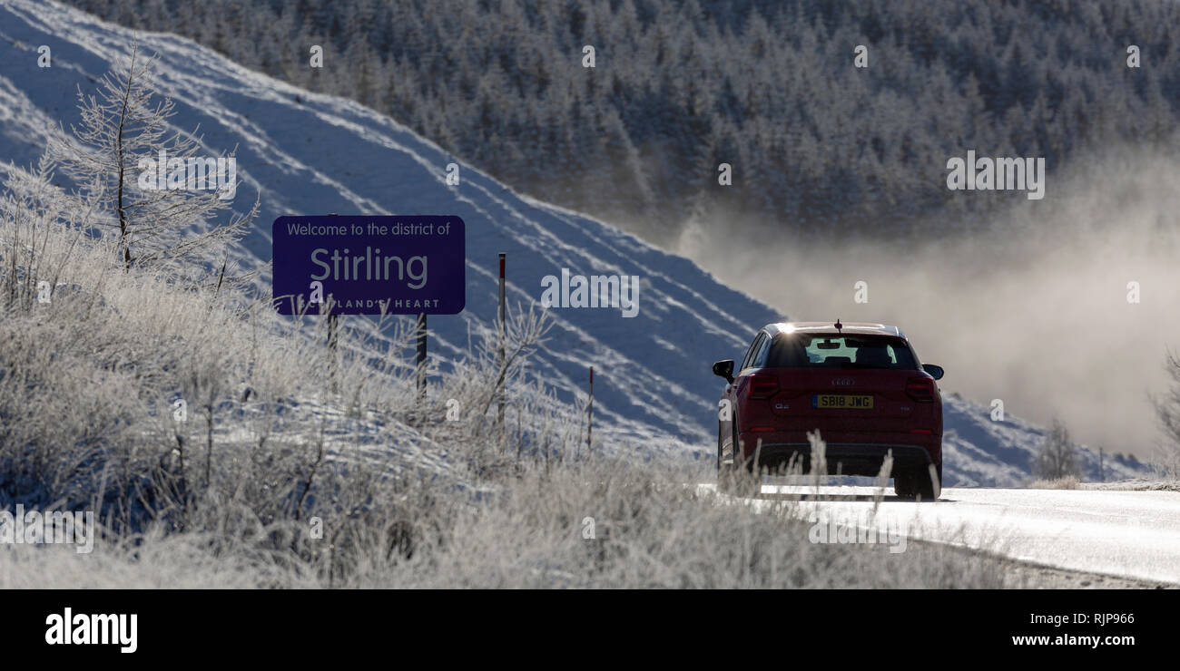 Red car on the A82 road entering the district of Stirling on a sunny day in winter, near Tyndrum, Scotland Stock Photo