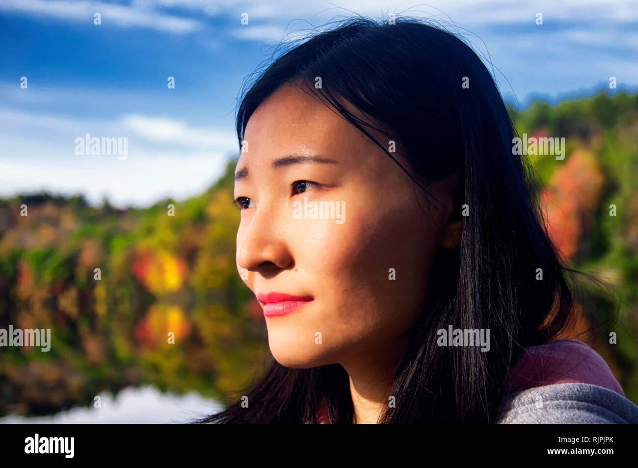 A beautiful chinese woman looking at the morning sunlight in autumn at Burr Pond state park in torrington, connecticut. Stock Photo
