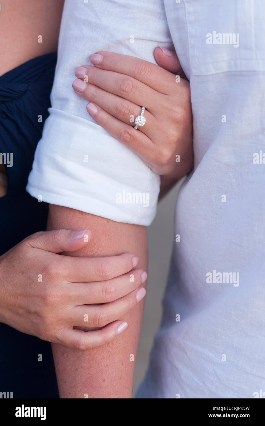 Close-up of an engaged young woman holding her fiance's arms at the beach during an engagement photoshoot. Stock Photo