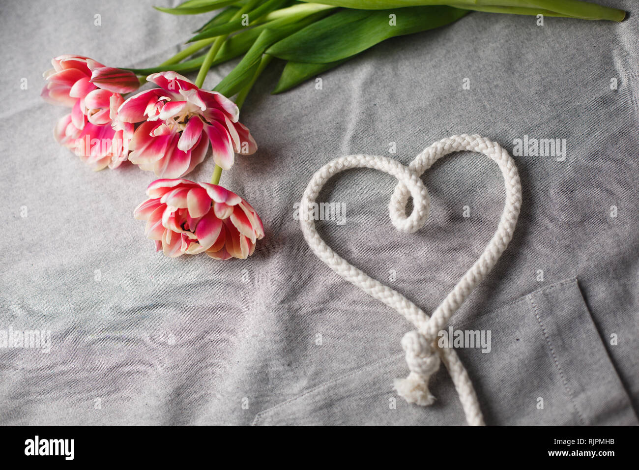Heart from rope and bouquet of tulips on a gray background with space ...