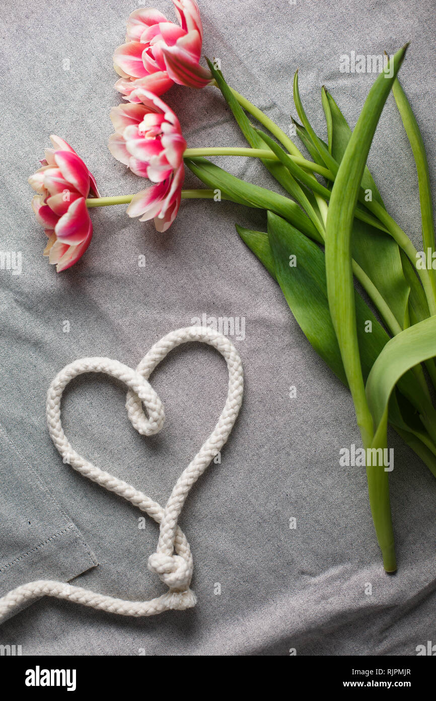 Heart from rope and bouquet of tulips on a gray background with space ...