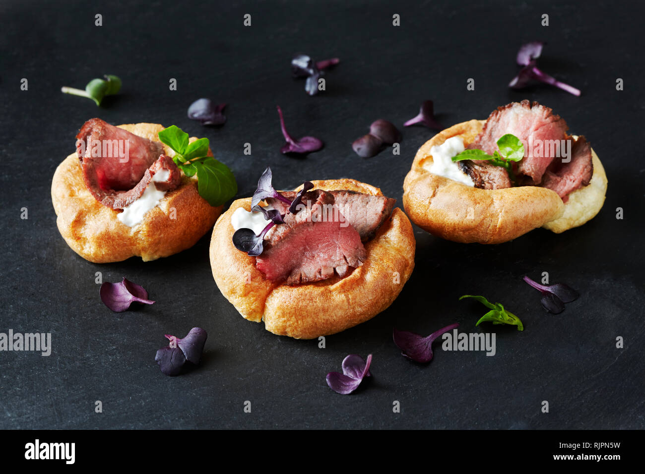 Still life with canapes of roast beef in yorkshire puddings on black