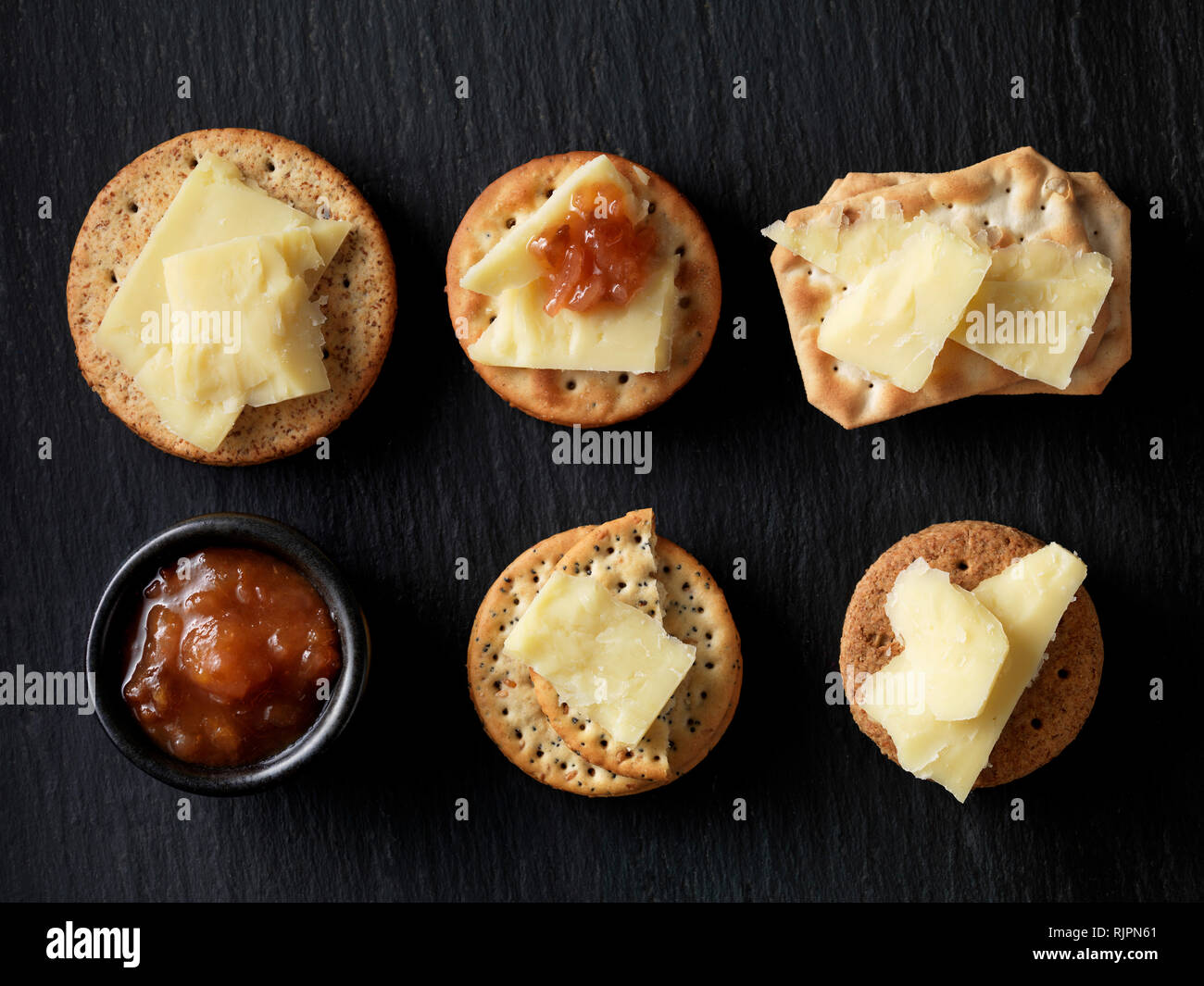 Still life of variety of cheese crackers with cheddar cheese and chutney on black slate, overhead view Stock Photo