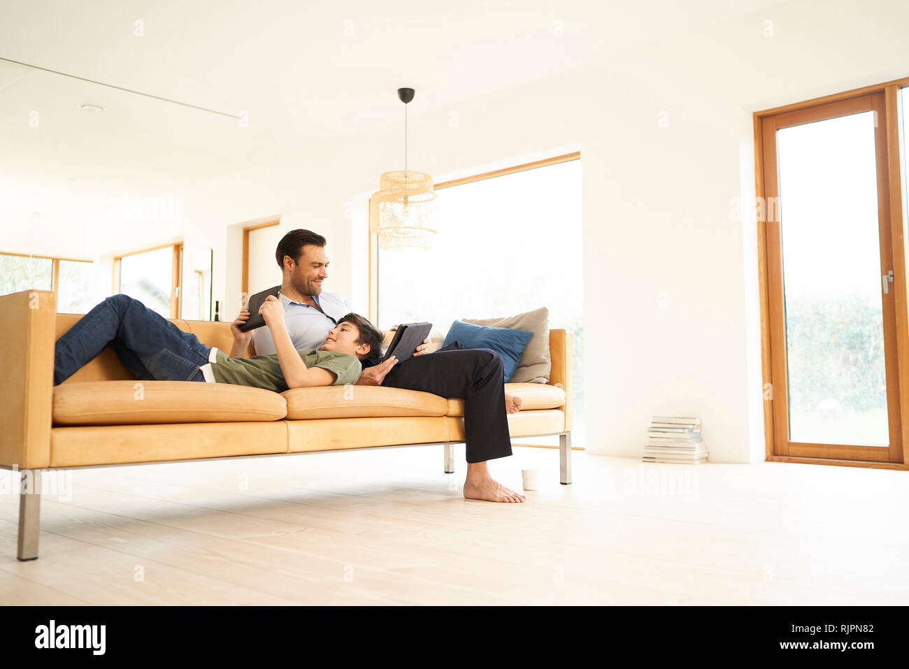 Boy and father using digital tablets whilst reclining on sofa Stock Photo