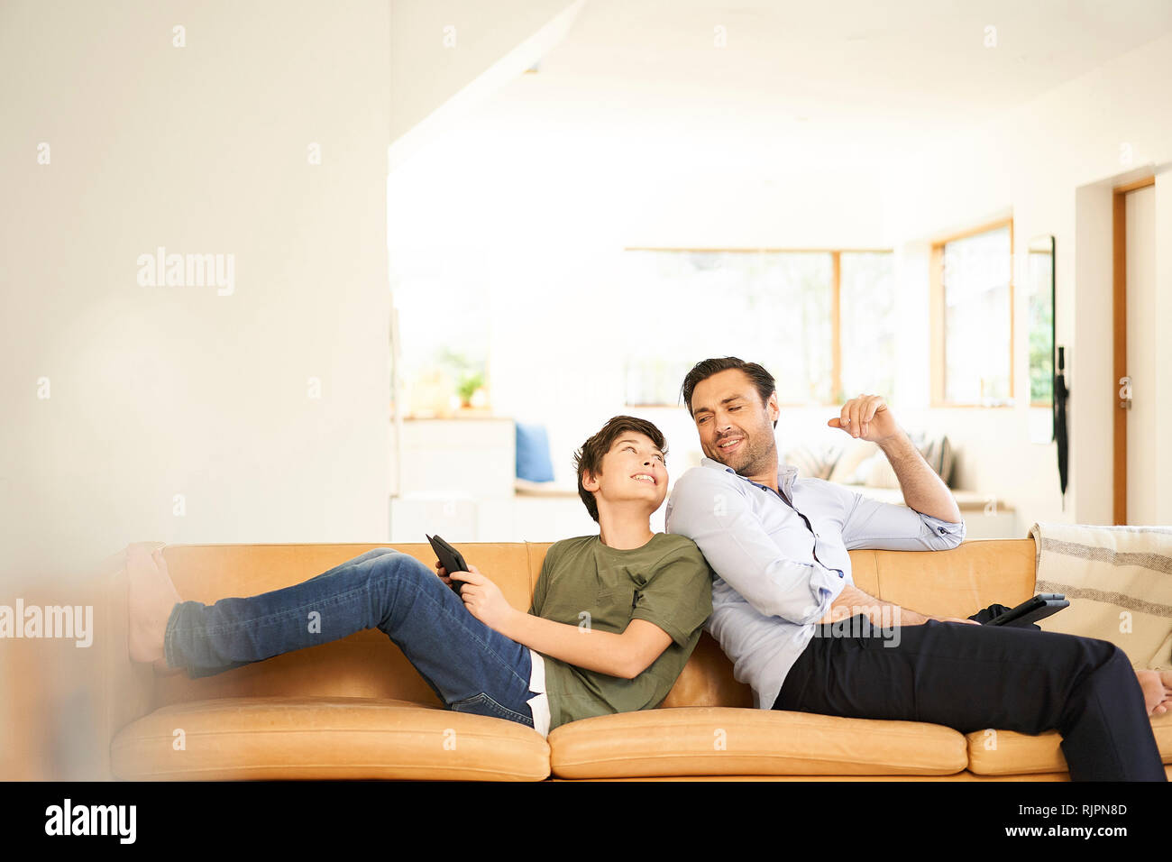 Boy and father using digital tablets back to back on sofa Stock Photo
