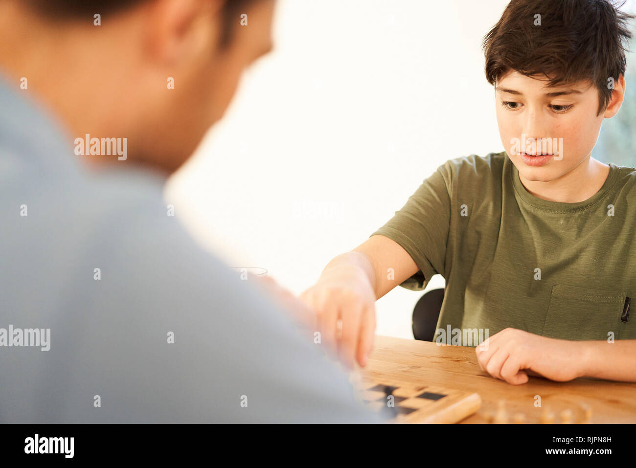 Boy and father playing chess at living room table,over shoulder view Stock Photo