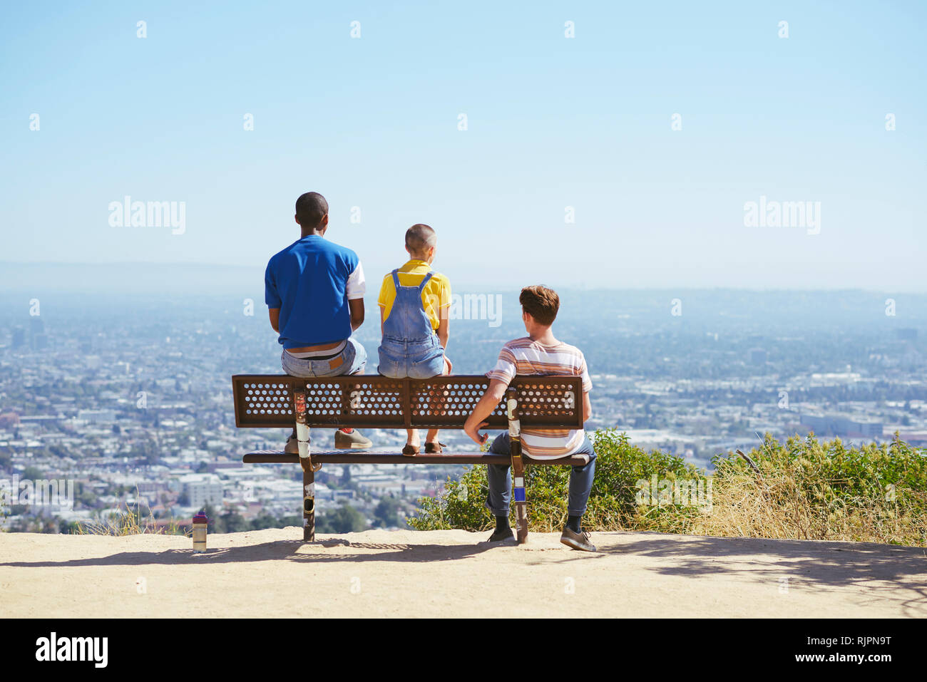 Three young adult friends on cityscape hilltop bench, rear view, Los Angeles, California, USA Stock Photo