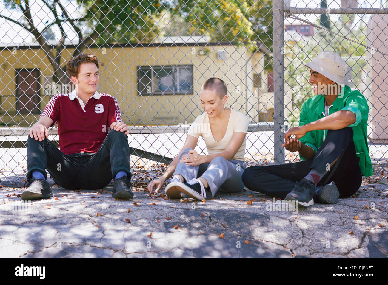 Three young adult friends sitting by park fence, Los Angeles, California, USA Stock Photo