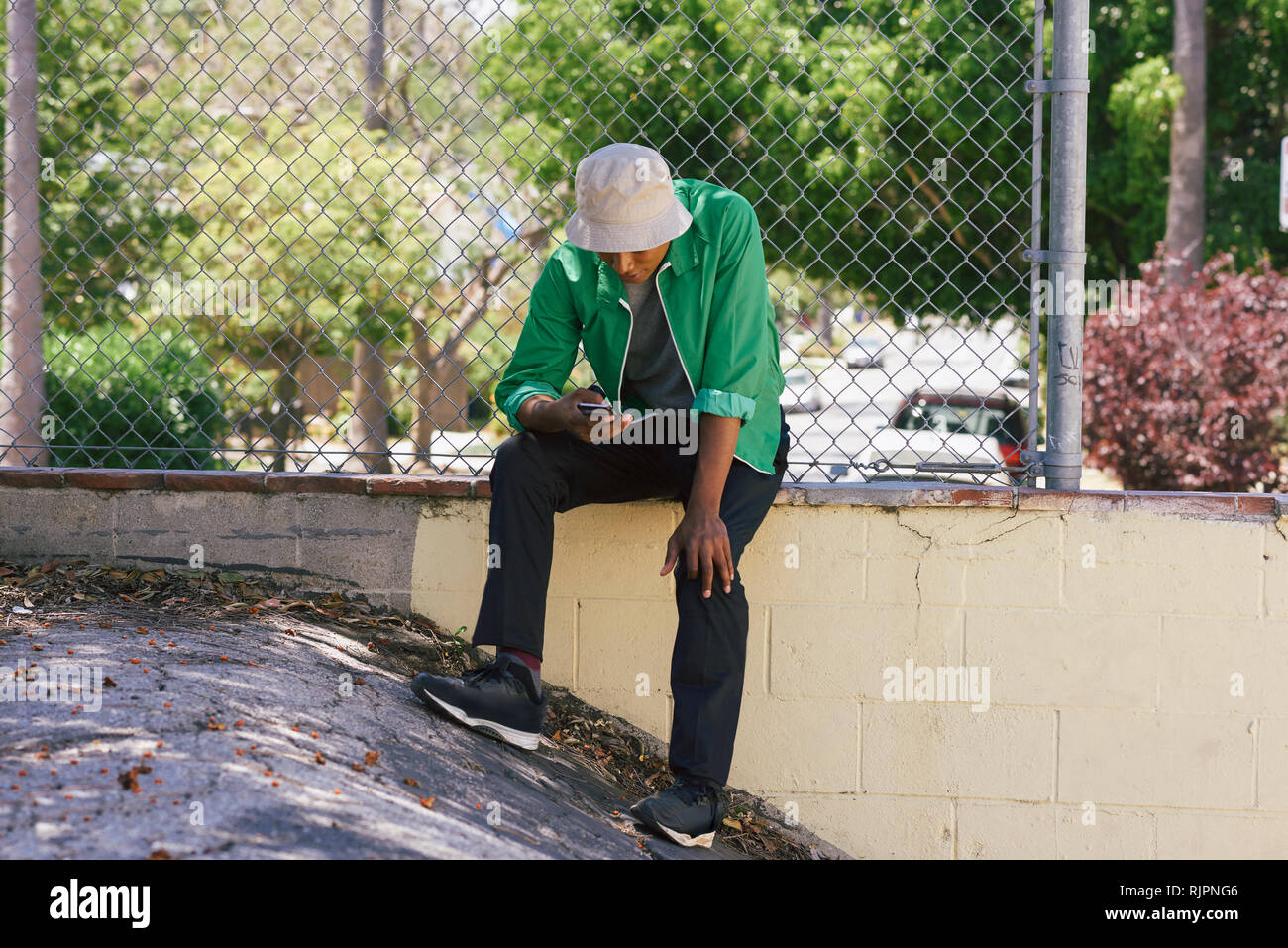 Young man looking at smartphone by park fence, Los Angeles, California, USA Stock Photo