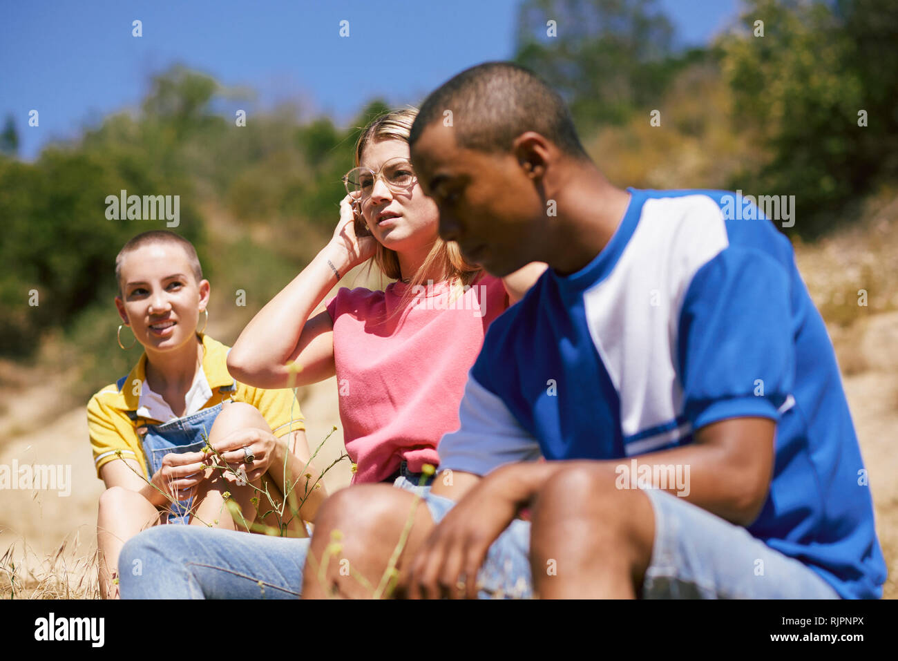 Three young adult friends sitting by dirt track, Los Angeles, California, USA Stock Photo