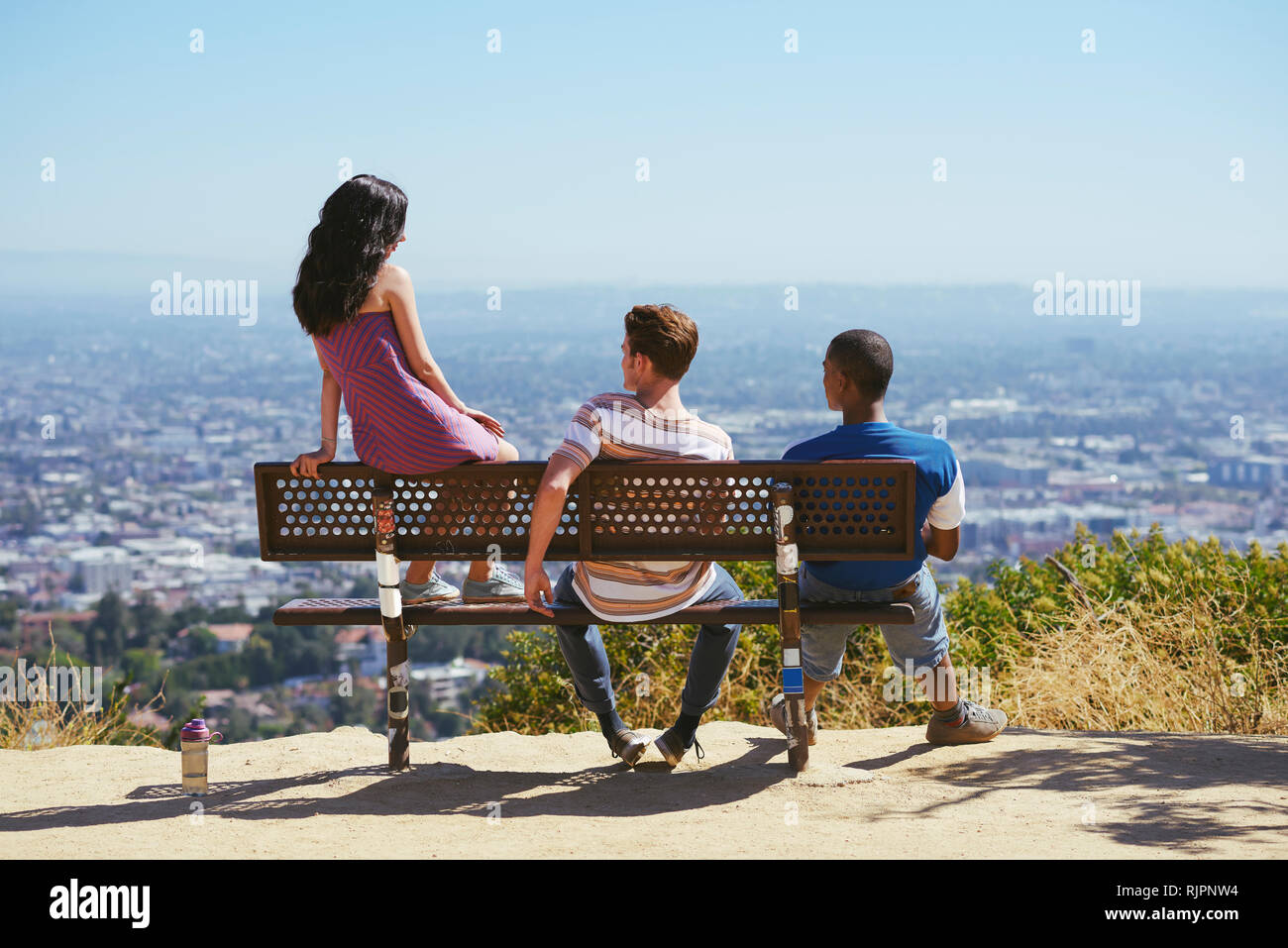 Three young adult friends looking out at cityscape from hilltop bench, rear view, Los Angeles, California, USA Stock Photo