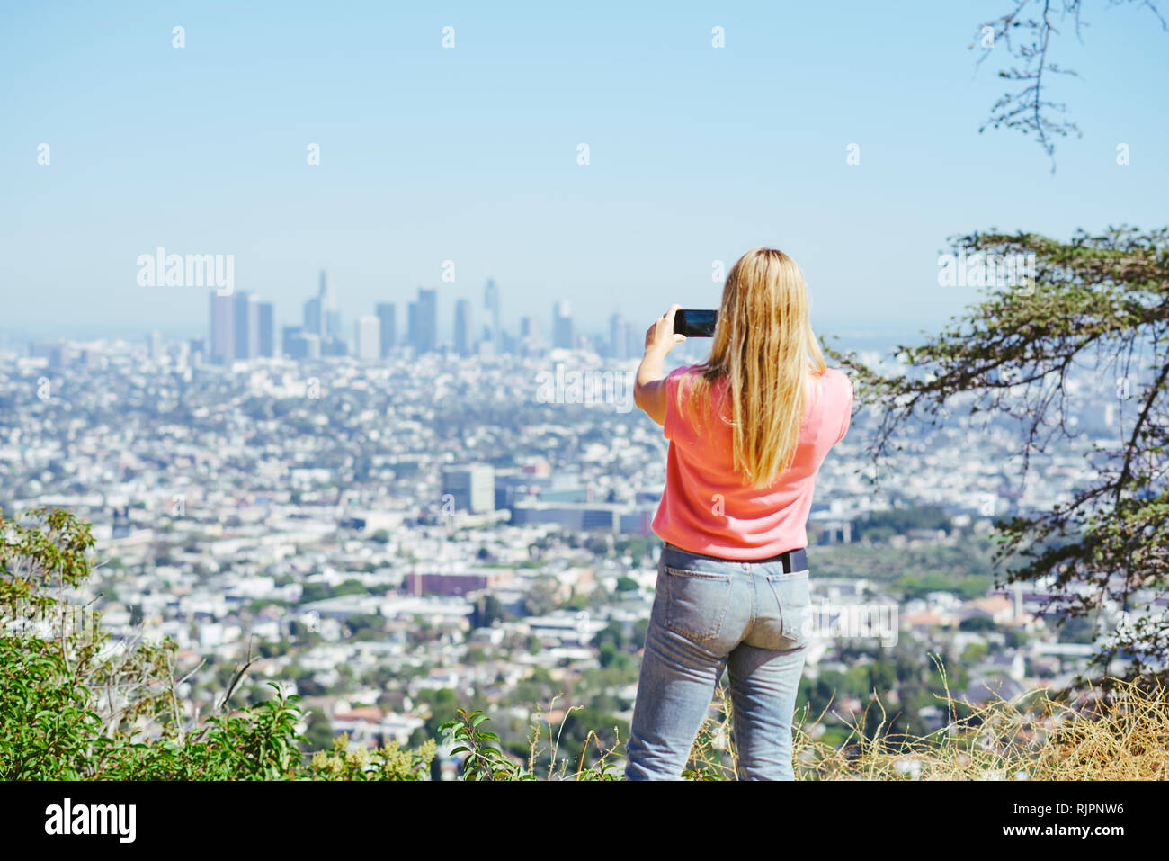 Young woman photographing skyline from hilltop, rear view, Los Angeles, California, USA Stock Photo