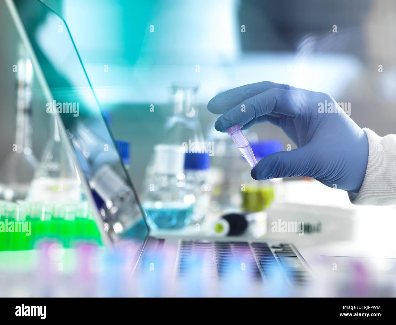 Scientist examining vial containing sample used in biomedical, DNA, biotechnology, analytical chemistry, pharmaceutical research Stock Photo