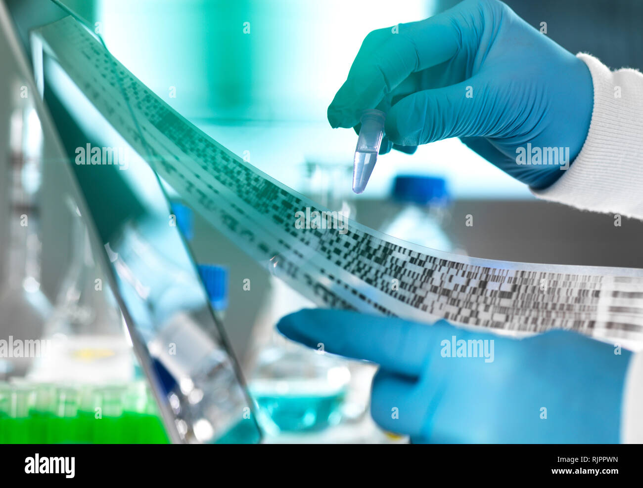 Research scientist holding a sample in a vial with DNA results on autoradiogram gel in laboratory, close up of hand Stock Photo