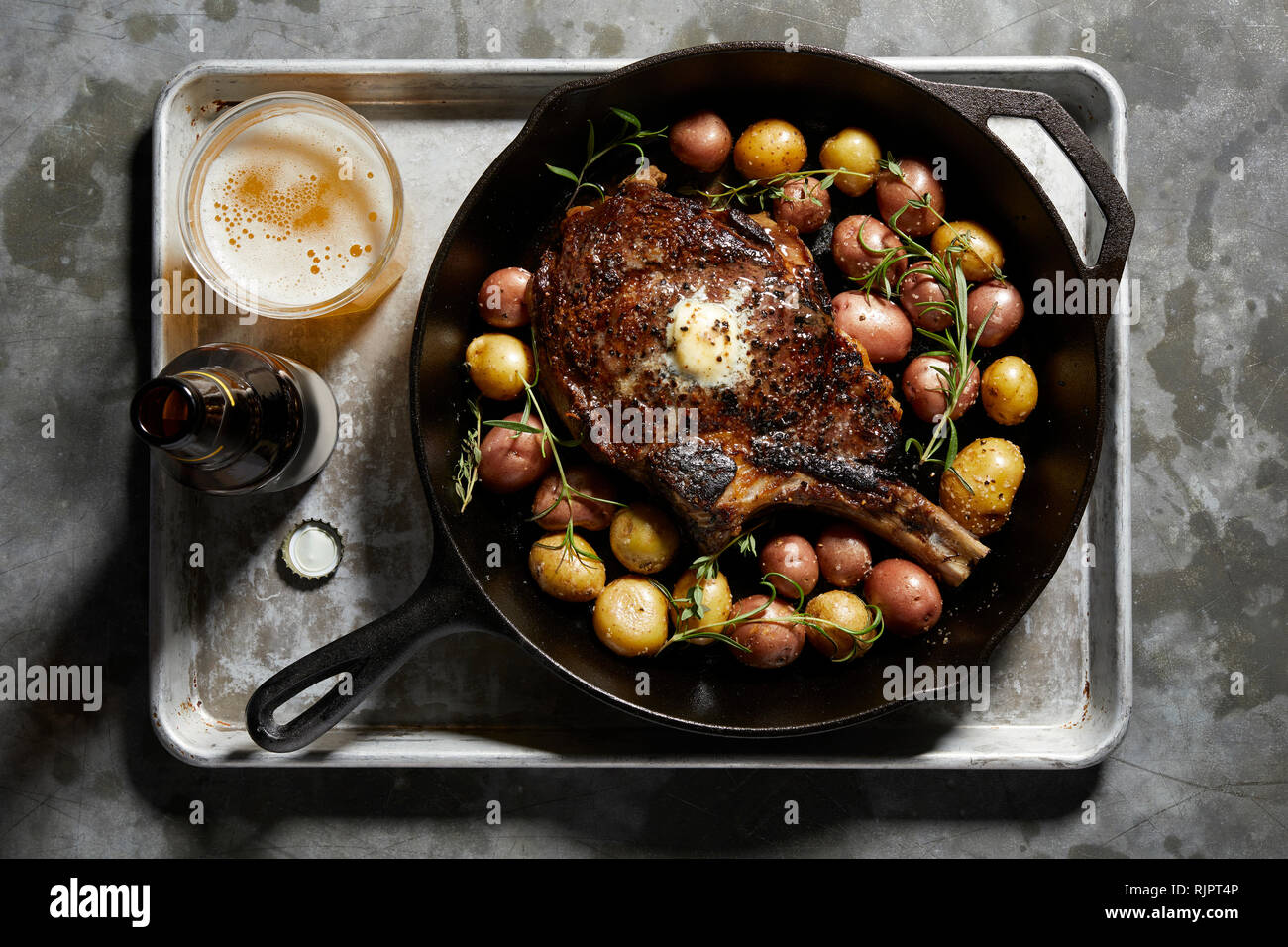 Skillet with large tomahawk steak & potatoes, overhead view Stock Photo