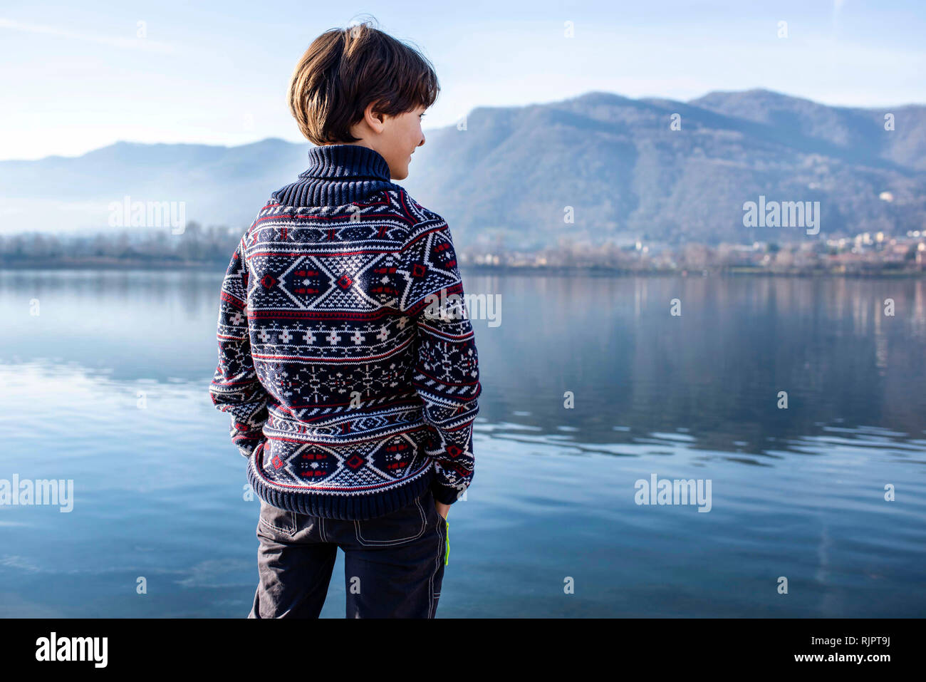 Boy looking out from lakeside, rear view, Lake Como, Lecco, Lombardy, Italy Stock Photo