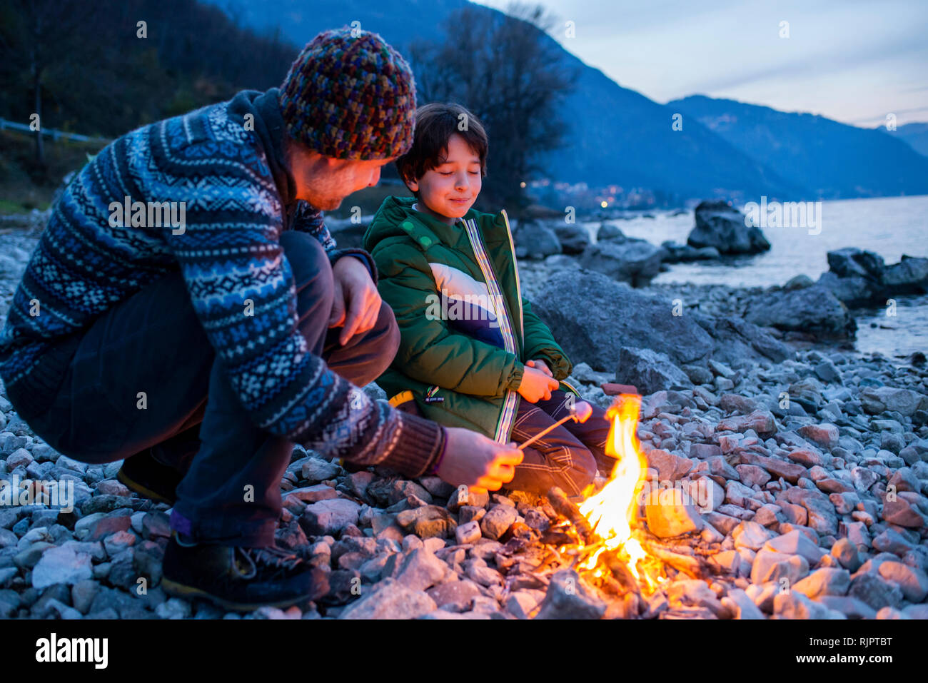 Father and son toasting marshmallows over campfire, Onno, Lombardy, Italy Stock Photo