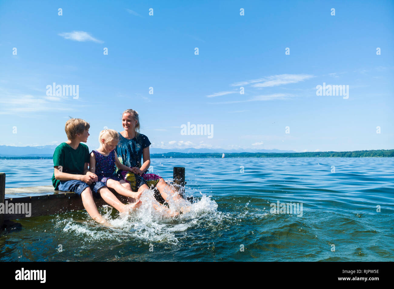 Mother and children cooling feet in water, Lake Starnberg, Bavaria, Germany Stock Photo