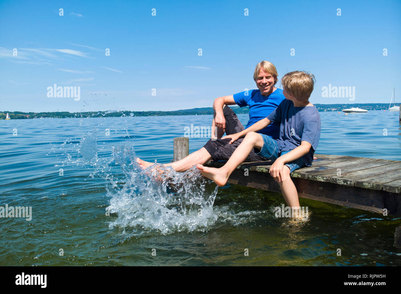 Father and son cooling feet in water, Lake Starnberg, Bavaria, Germany Stock Photo