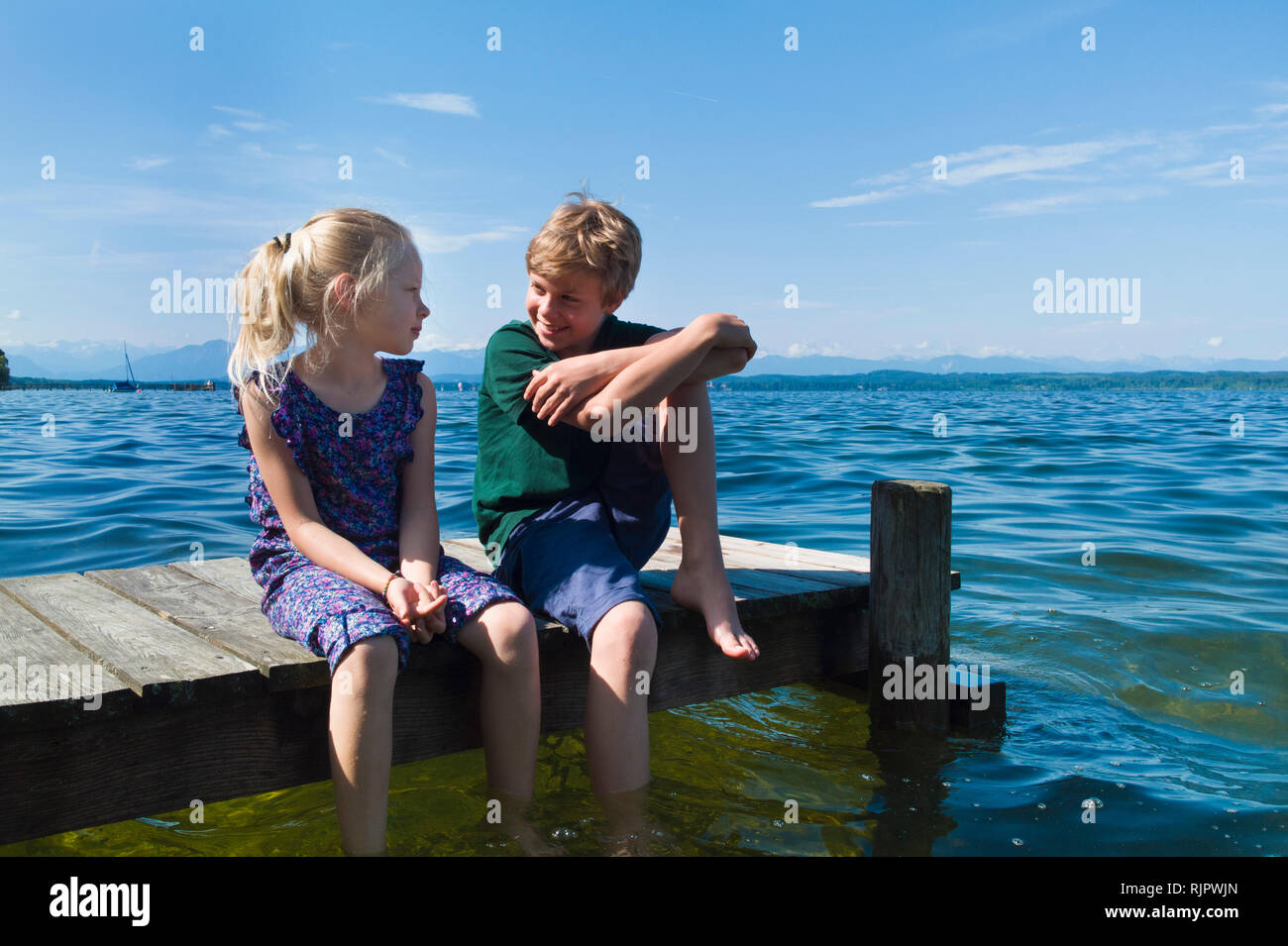 Siblings cooling feet in water, Lake Starnberg, Bavaria, Germany Stock Photo