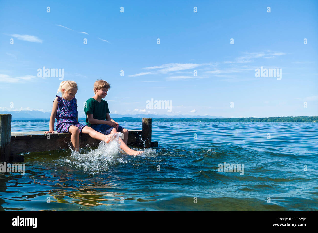 Siblings cooling feet in water, Lake Starnberg, Bavaria, Germany Stock Photo