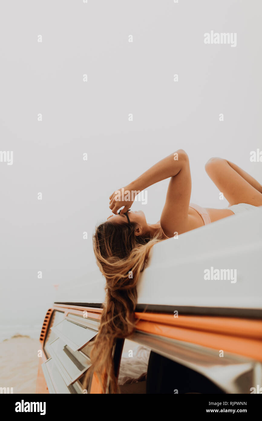 Young woman in bikini lying on top of recreational vehicle at beach, Jalama, California, USA Stock Photo