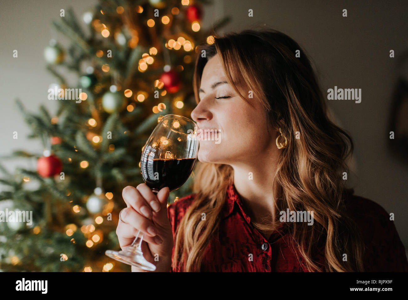 Woman smelling glass of wine beside decorated Christmas tree Stock Photo