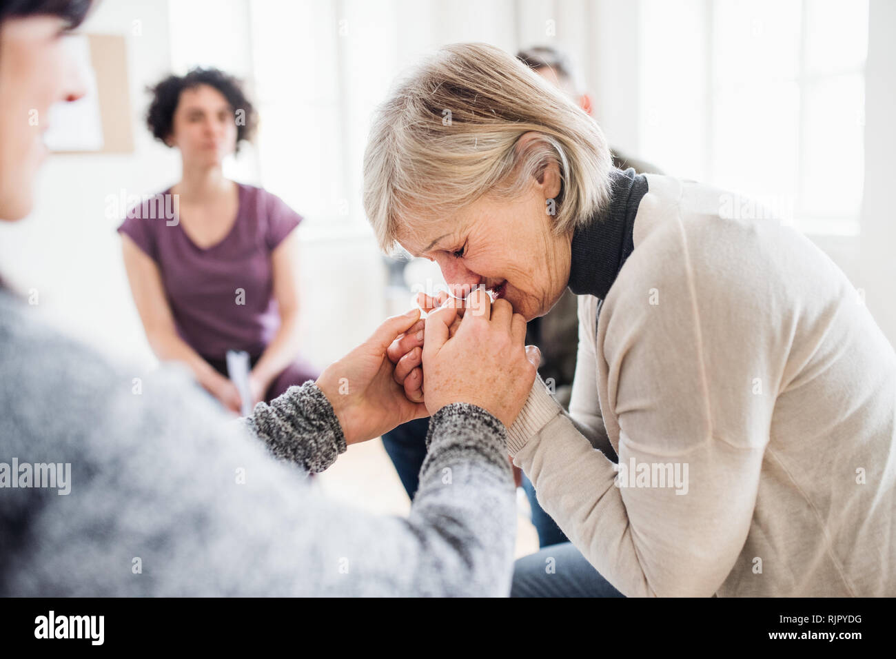 A senior depressed woman crying during group therapy. Stock Photo