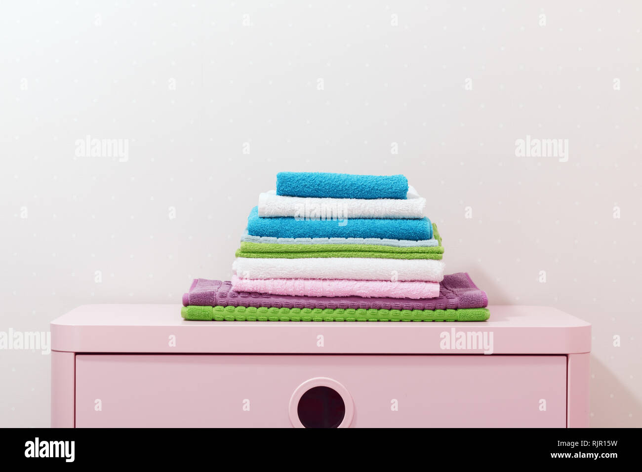 On the chest lies a stack of stacked colorful towels. Stock Photo