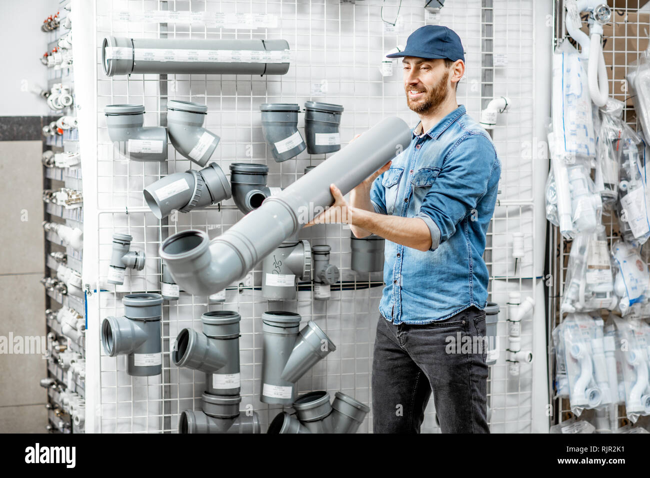 Handsome workman choosing sewer pipes standing near the showcase of the