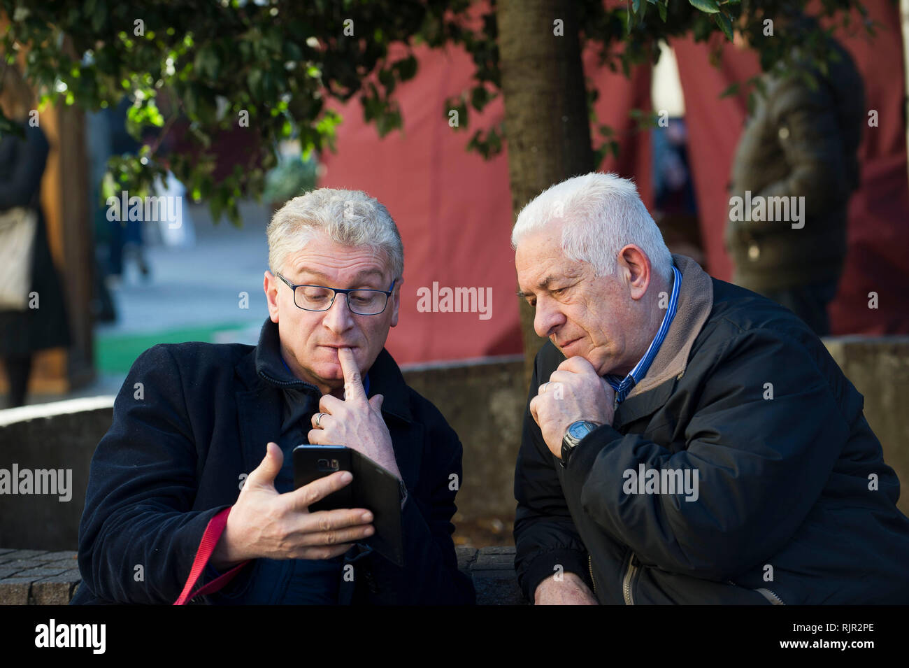 Italy, Lombardy, Monza, the elderly on the bench study how a mobile phone works Stock Photo