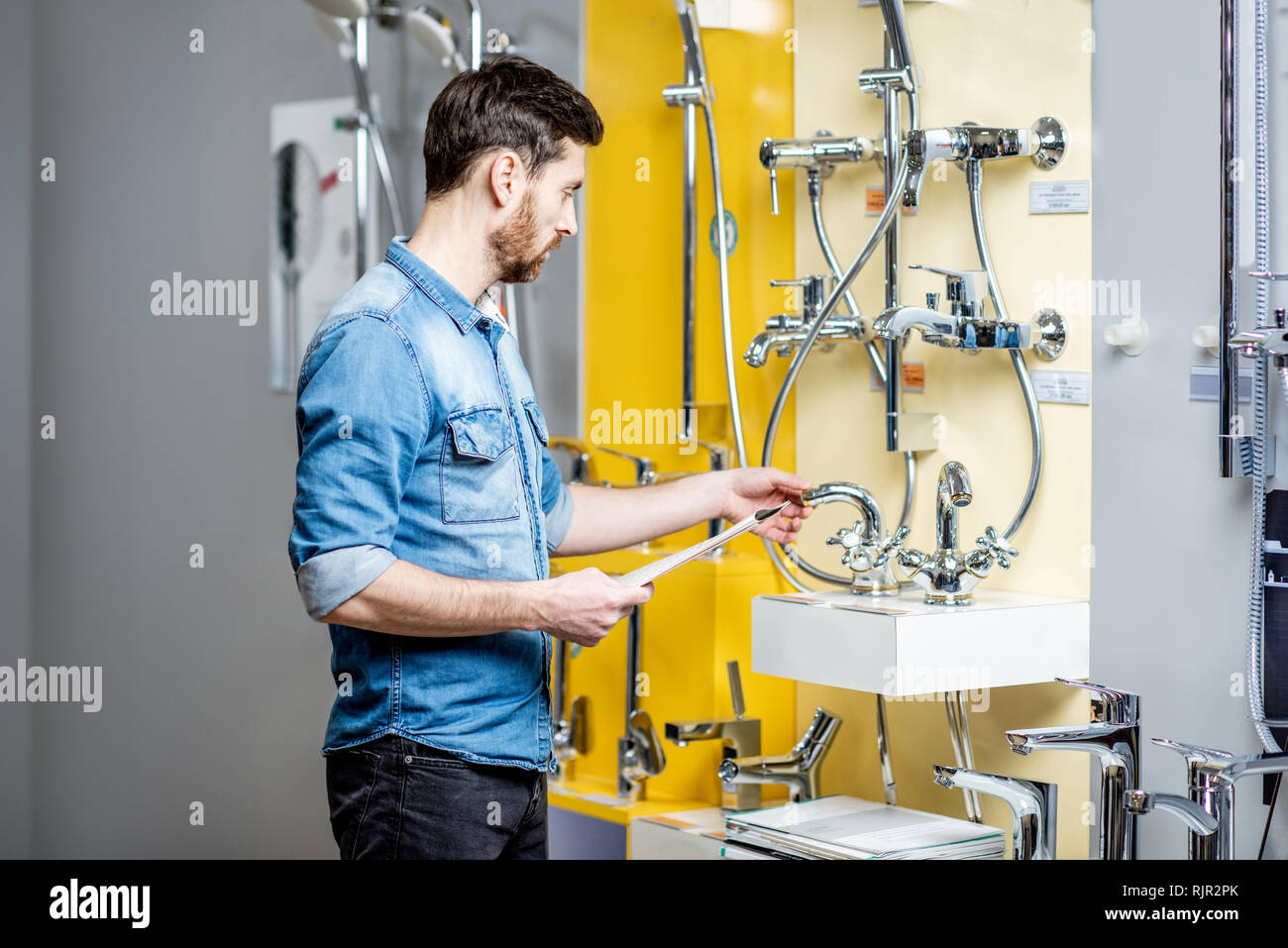 Man choosing shower faucet standing near the beautiful showcase of the plumbing shop Stock Photo