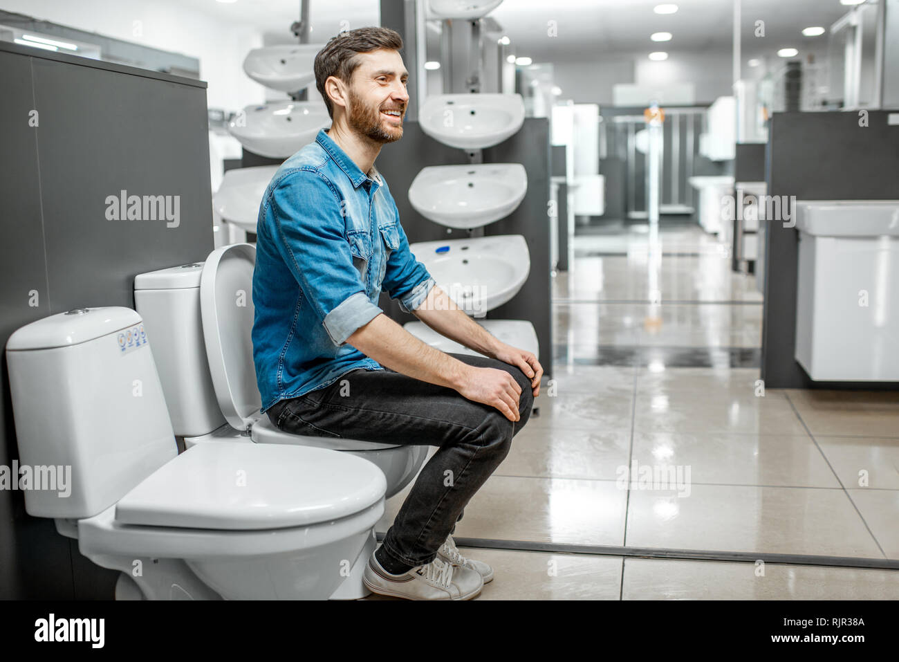Man choosing lavatory pan sitting on it in the building shop with sanitary ceramics Stock Photo