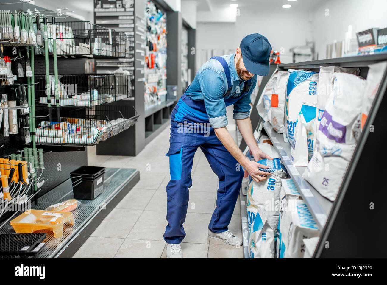 Workman in blue overalls taking a bag with construction mixture, buying materials for repairing in the building supermarket Stock Photo