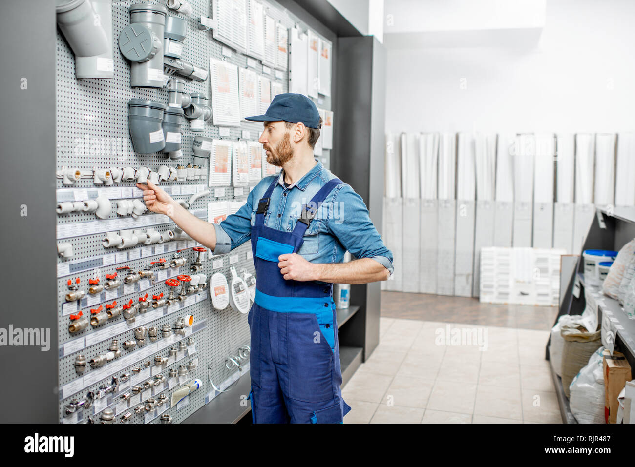 Handsome workman choosing water pipes and pipe joints standing near the showcase in the plumbing