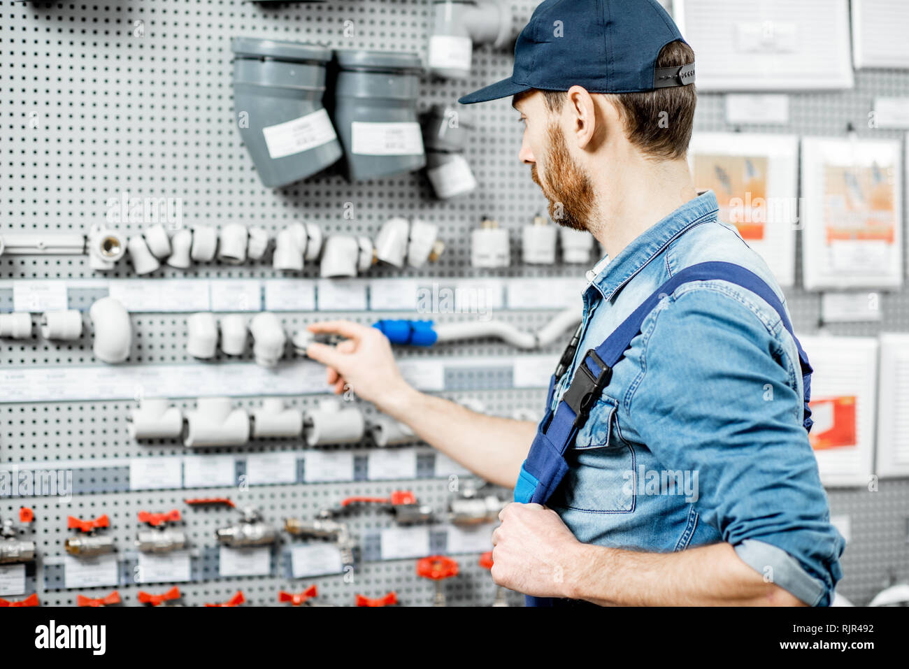Handsome workman choosing water pipes and pipe joints standing near the showcase in the plumbing