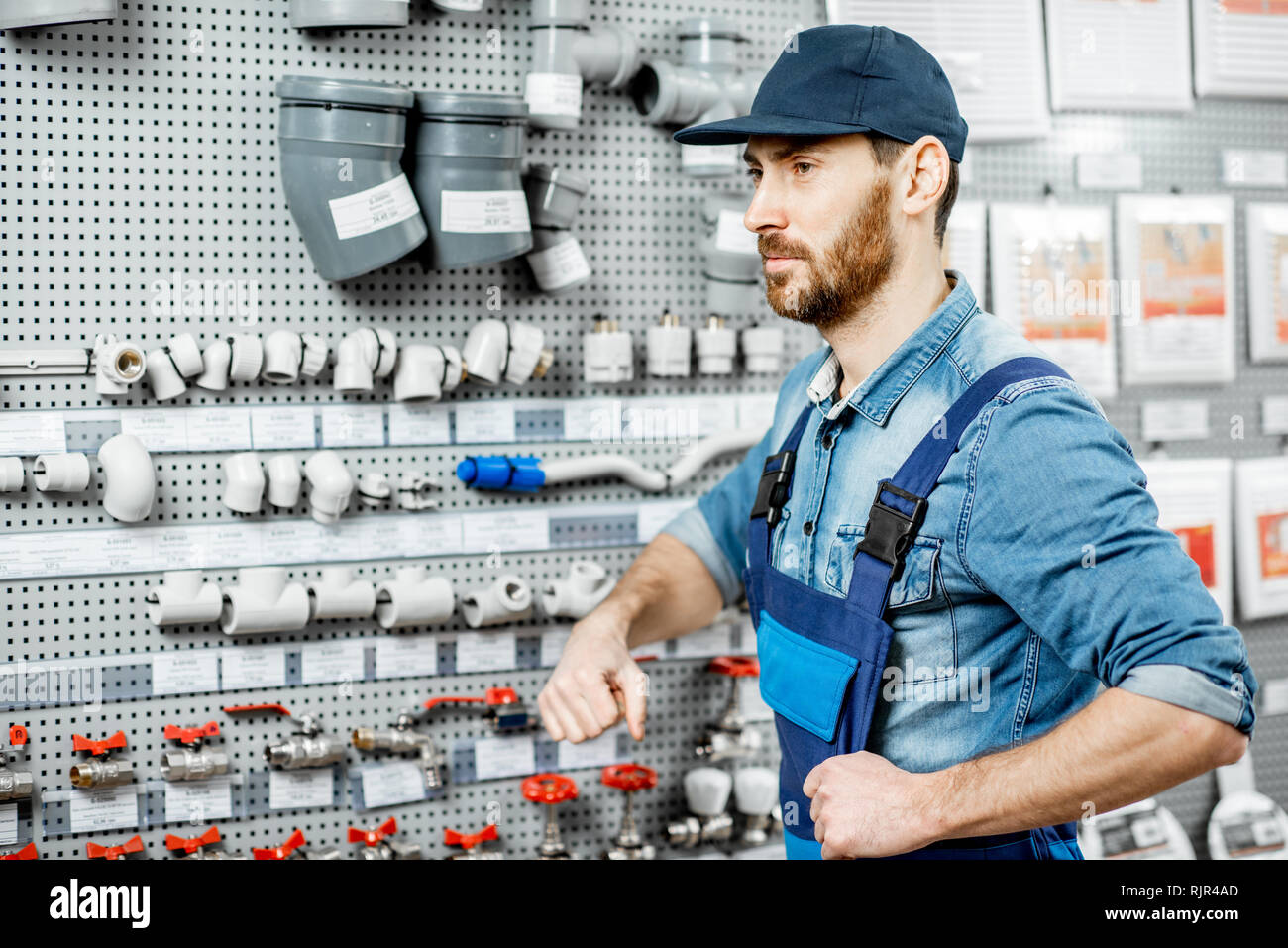 Handsome workman choosing water pipes and pipe joints standing near the