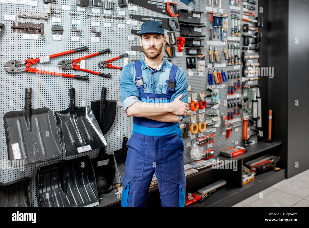 Portrait of a handsome worker in uniform standing in the shop with garden equipment on the background Stock Photo