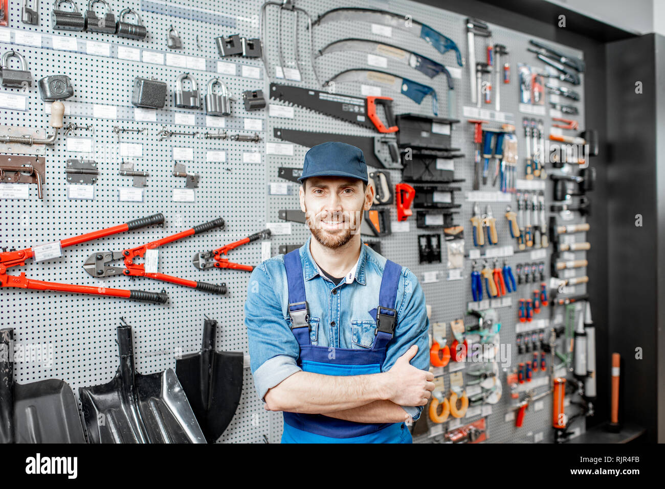 Portrait of a handsome worker in uniform standing in the shop with garden equipment on the background Stock Photo