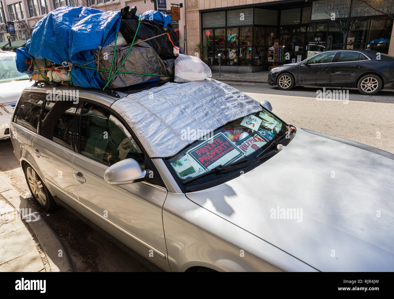 ASHEVILLE, NC, USA-2/3/19: A car has dashboard filled with signs and trash, and filled plastic bags tied on roof. Stock Photo