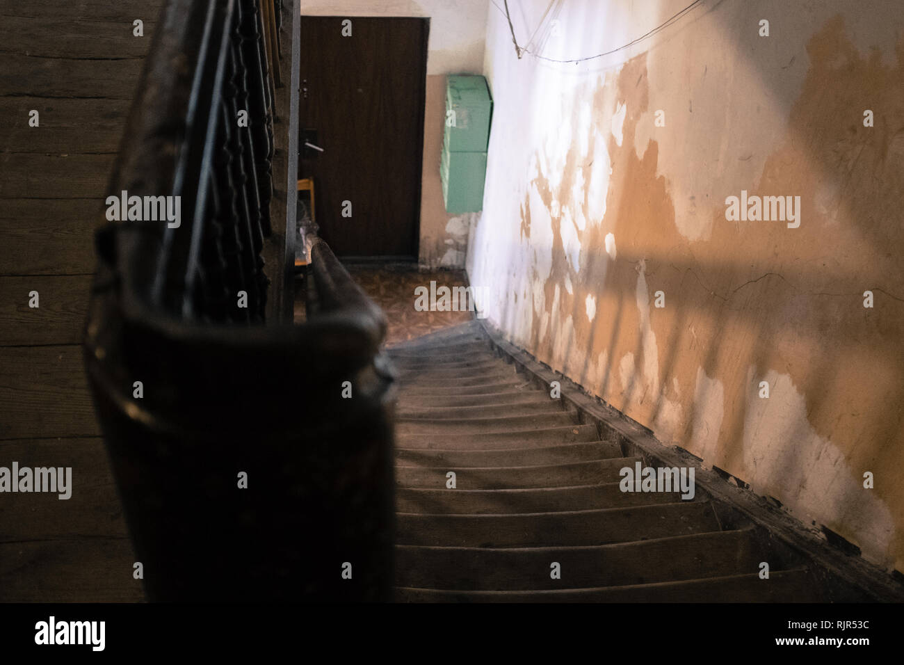 empty worn wooden staircase leading down to a door with shadows on the wall Stock Photo