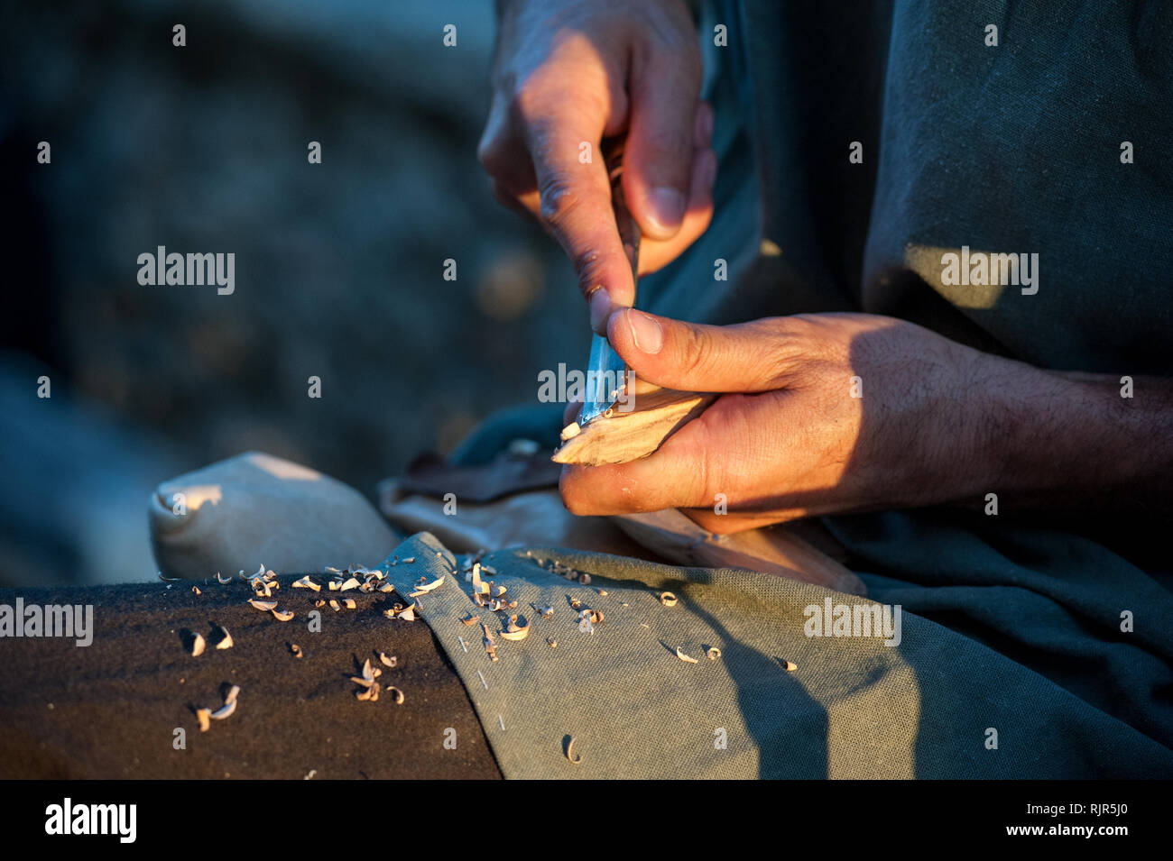 The artisan sharpens a wood stick, with a sharp blade Stock Photo