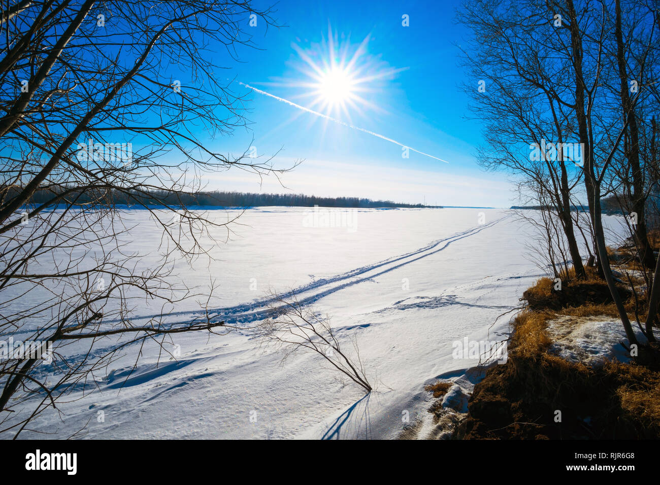 Traces of an airplane in the blue sky and from all-terrain vehicle on  frozen river . Stock Photo